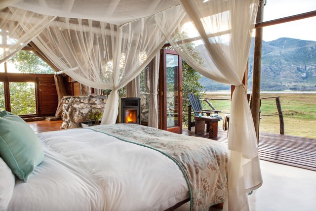 Four poster bed in the Kingfisher Room at Mosaic, Private Sanctuary, with a roaring fire in the background